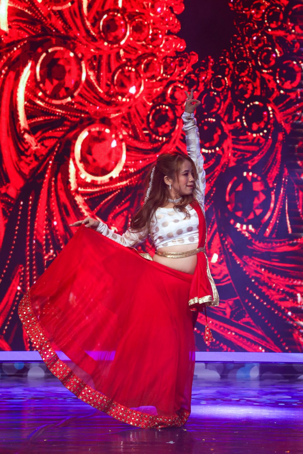 Amrita Rai making a joyful gesture in a red and white Bharatanatyam costume