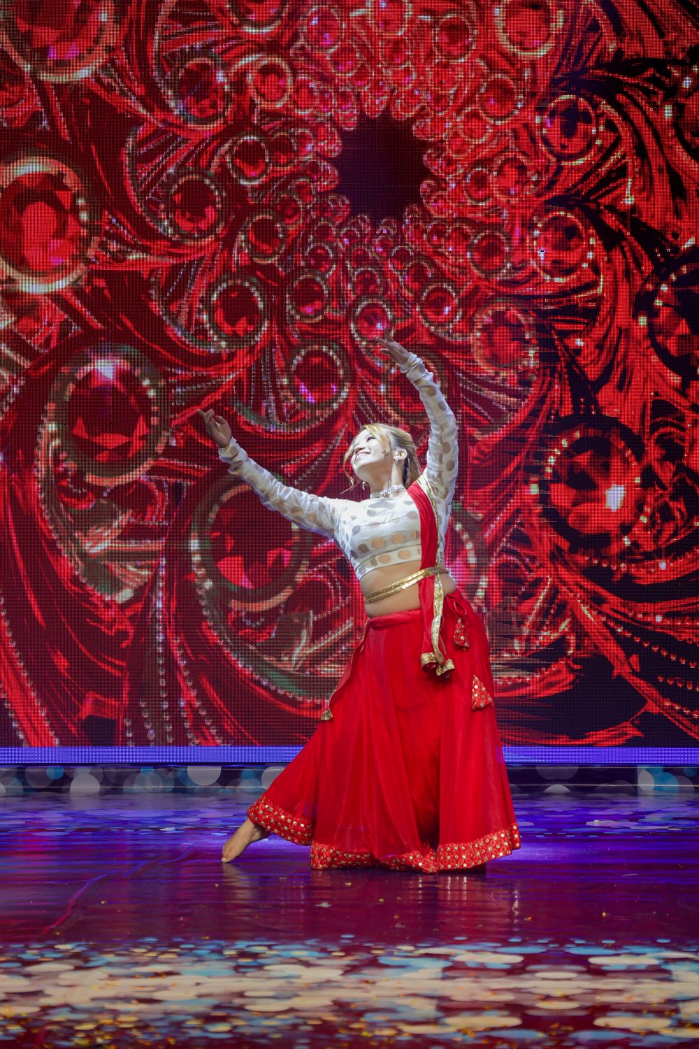 Amrita Rai spinning with arms raised in a red and white Bharatanatyam costume